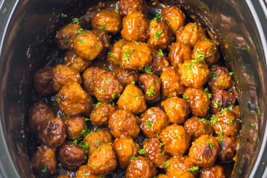 low cooker filled with sticky Coca-Cola meatballs topped with parsley.