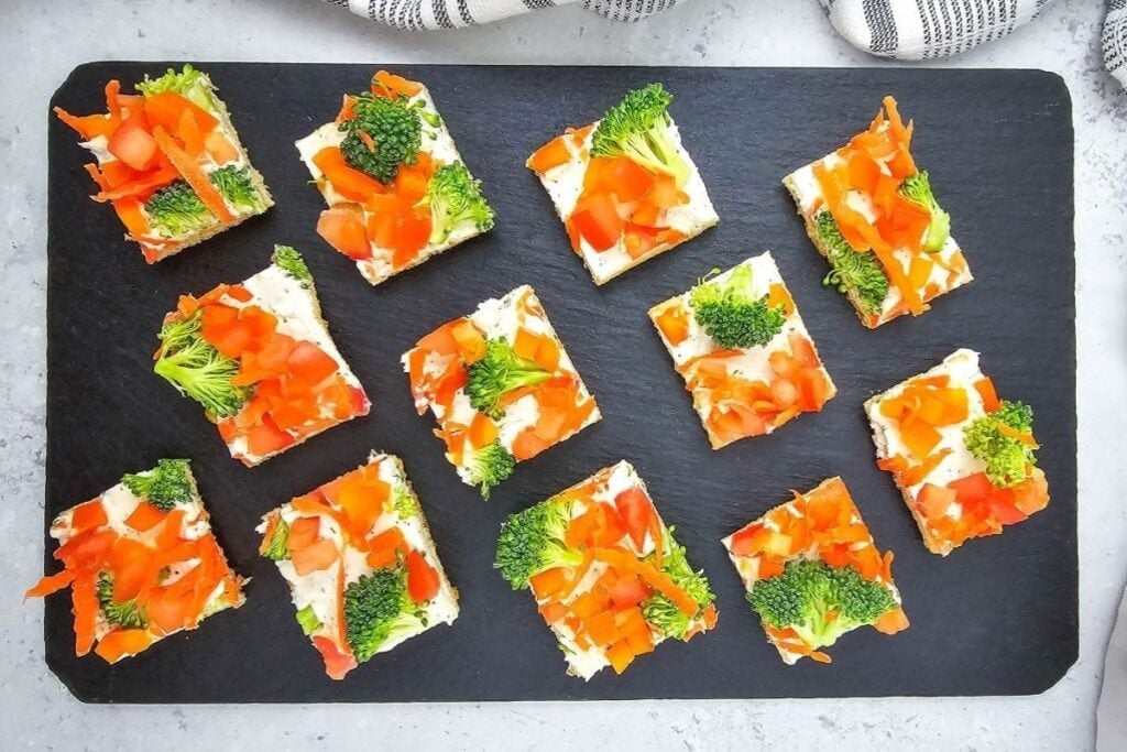 Crescent roll veggie pizza on a black slate plate topped with colorful vegetables.