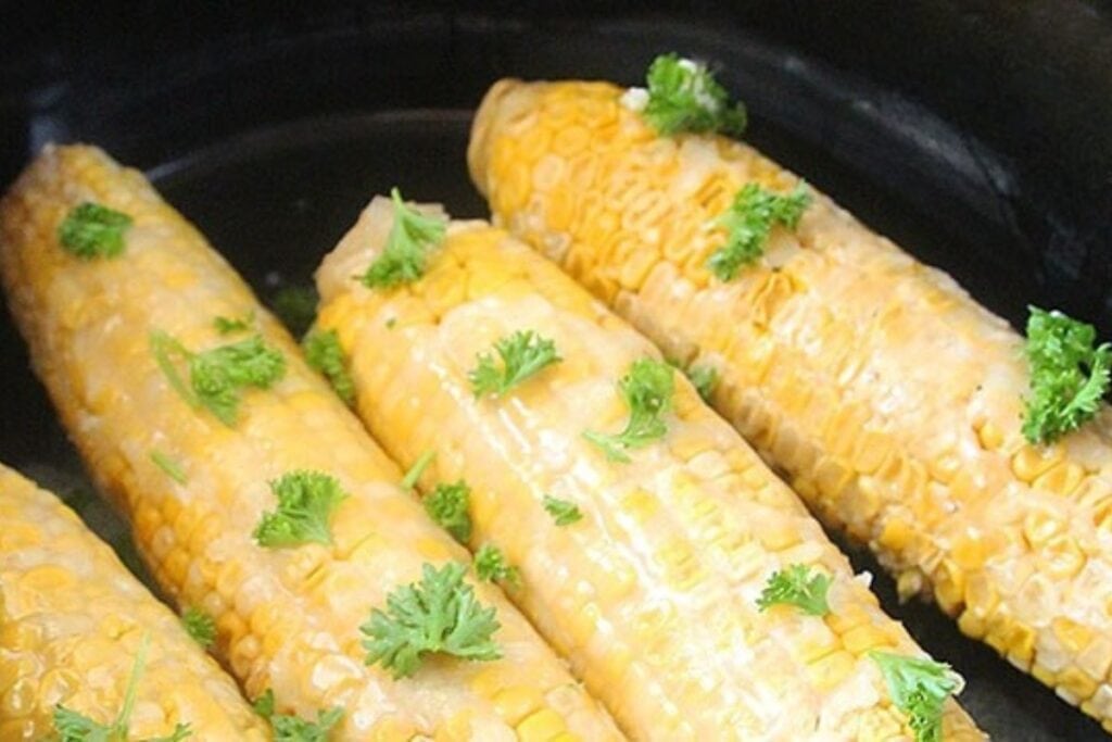 Crockpot corn on the cob topped with melted butter and parsley.