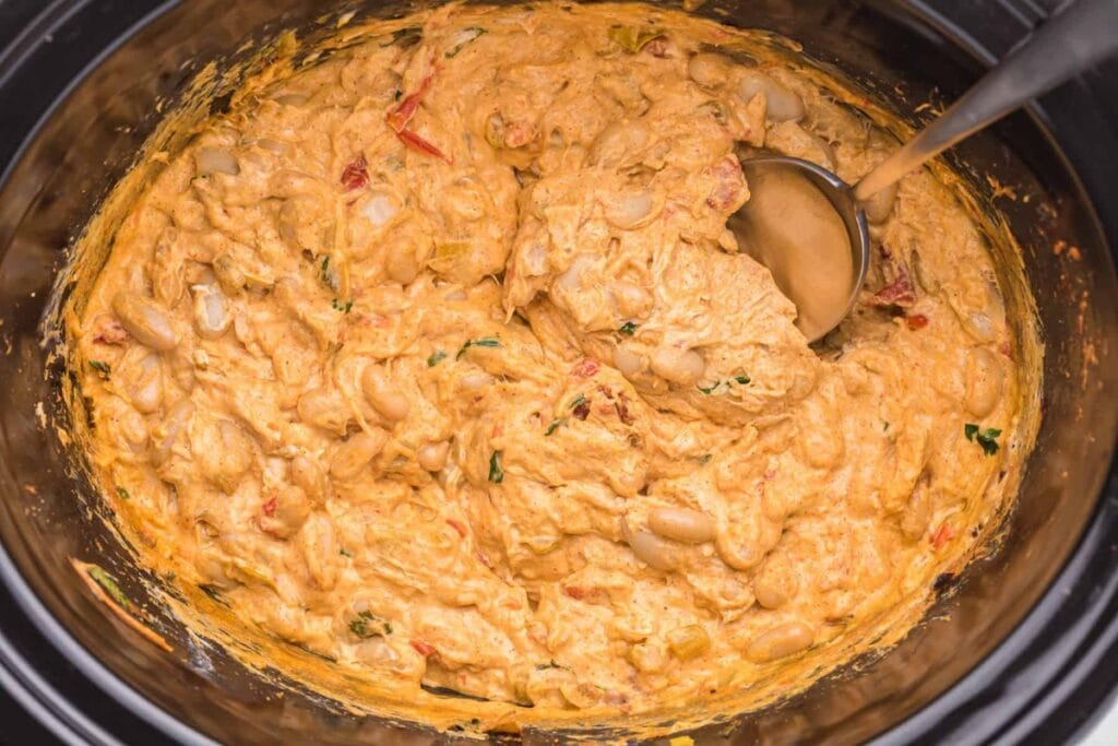 Creamy white chili chicken dip in a crockpot, with a spoon.