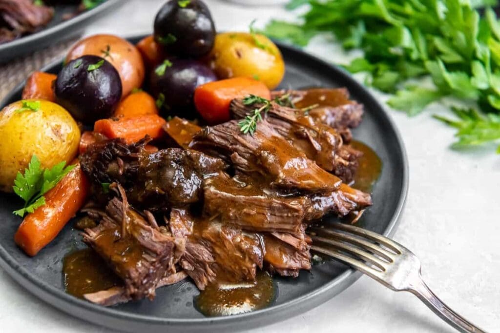 Dutch Oven Pot Roast served on a plate with carrots, potatoes, and gravy.