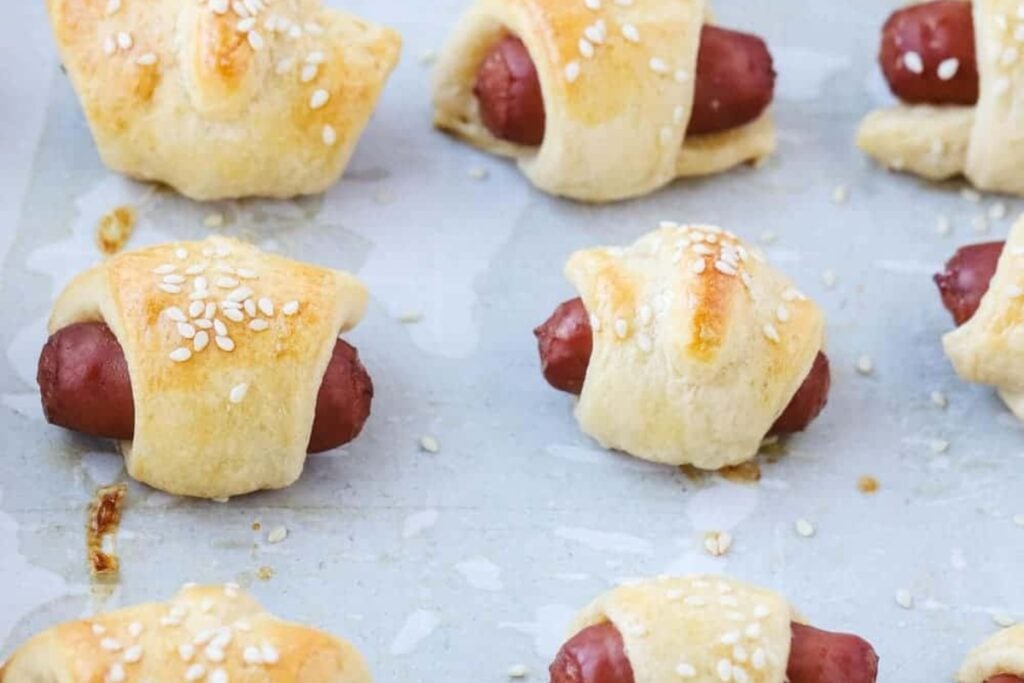 Golden garlic Parmesan pigs in a blanket arranged on a parchment-lined sheet pan.