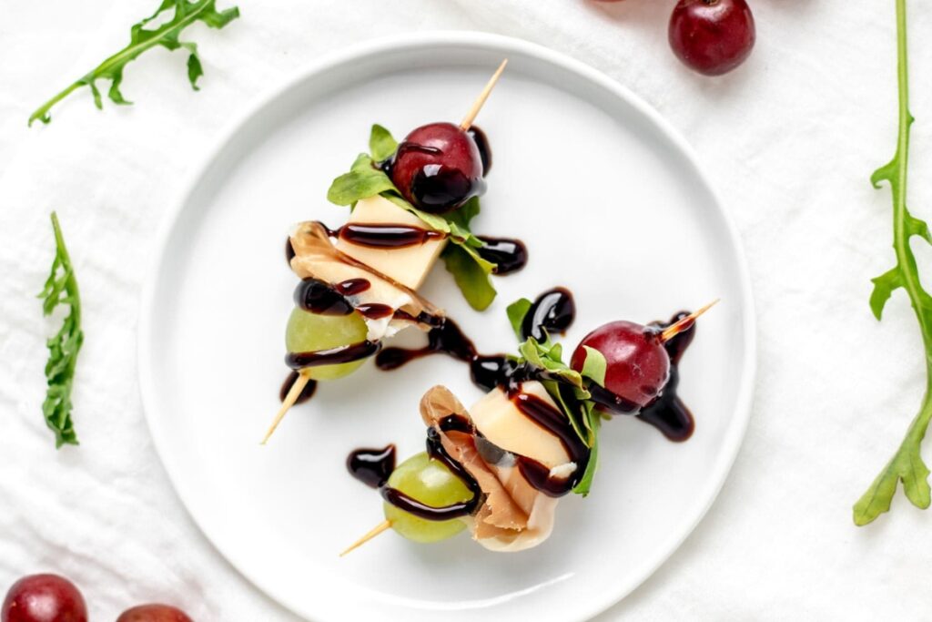 Grape, gouda, and arugula skewers on a plate, drizzled with balsamic glaze.