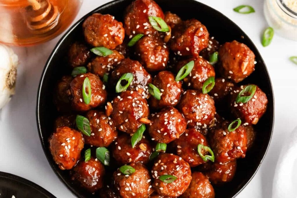 Honey garlic meatballs on a plate coated in a glossy sauce.