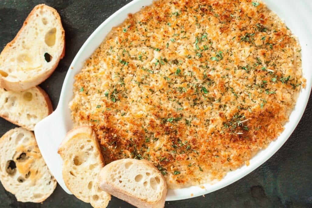 Jalapeño popper dip in a white baking dish with toasted bread slices on the side.