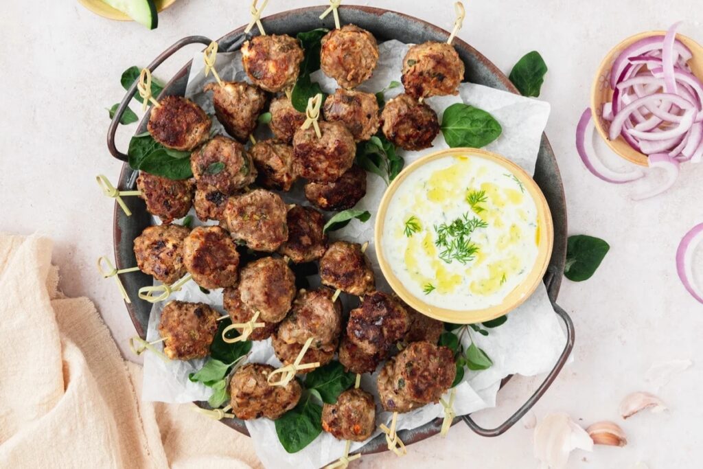 Lamb meatballs on a skillet with dipping sauce on the side.