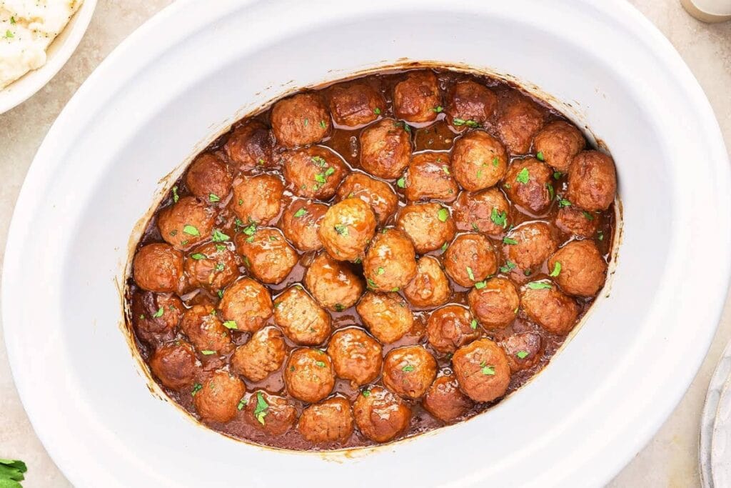 Meatballs in rich brown gravy inside a slow cooker.