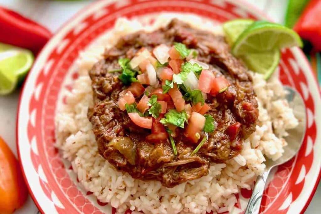 Mexican shredded beef served over rice on a plate.