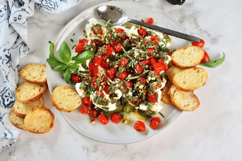 Burrata cheese with roasted tomatoes and basil pesto on a plate.