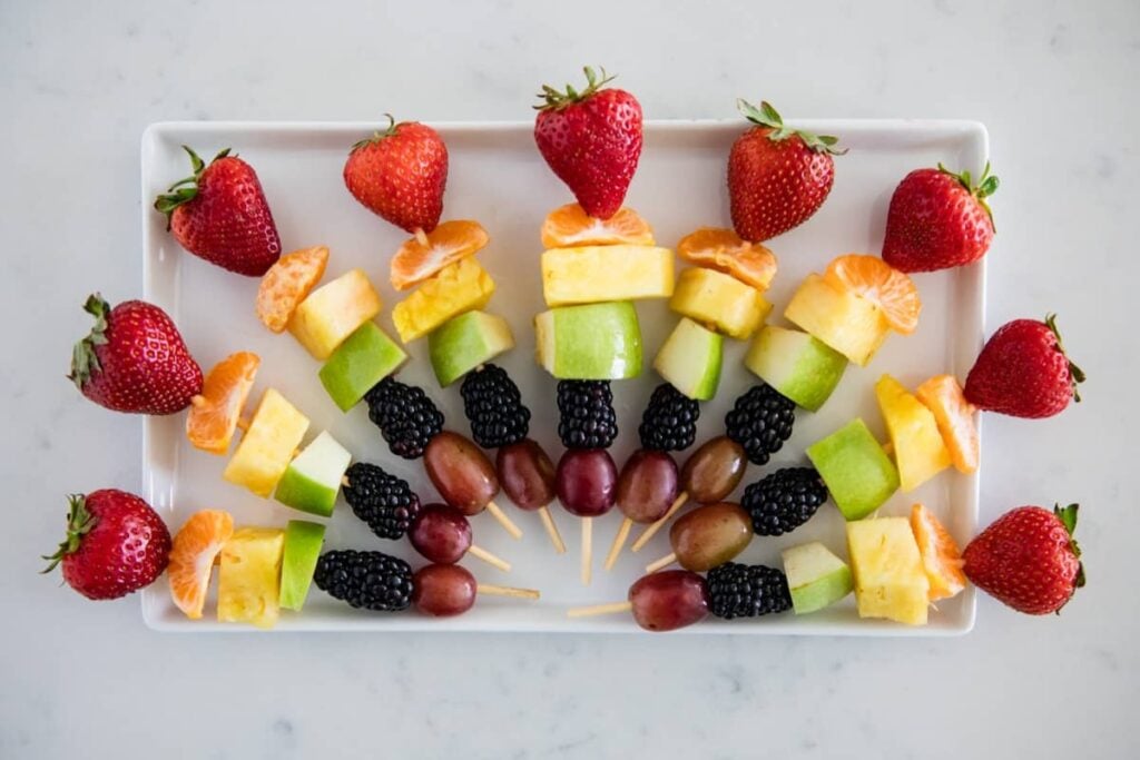 Colorful fruit kabobs arranged on a plate.