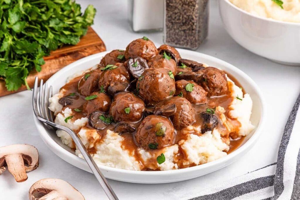 Salisbury steak meatballs served over mashed potatoes with gravy and mushrooms.
