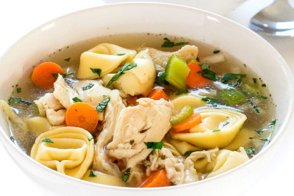 Chicken tortellini soup in a white bowl.