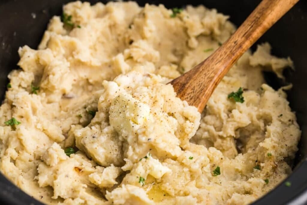 Slow cooker mashed potatoes stirred with a wooden spoon.
