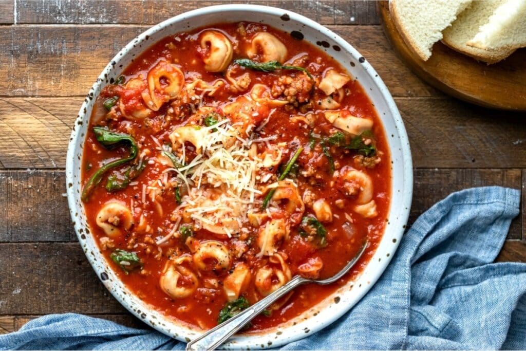Slow cooker tortellini soup in a bowl topped with cheese.
