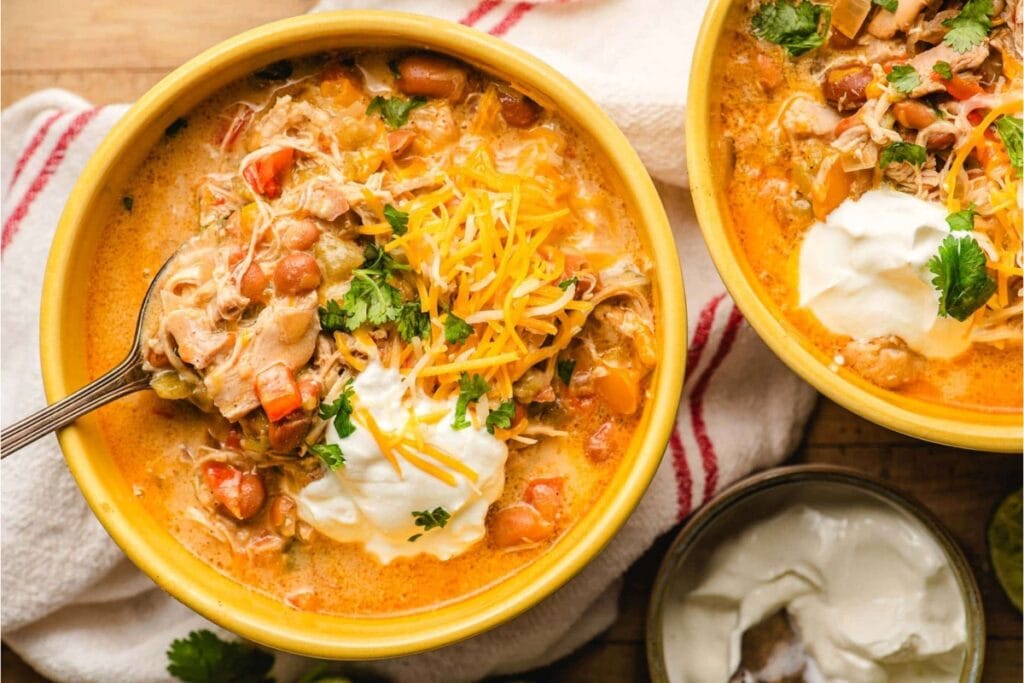 White chicken chili topped with cheese and sour cream in a yellow bowl.