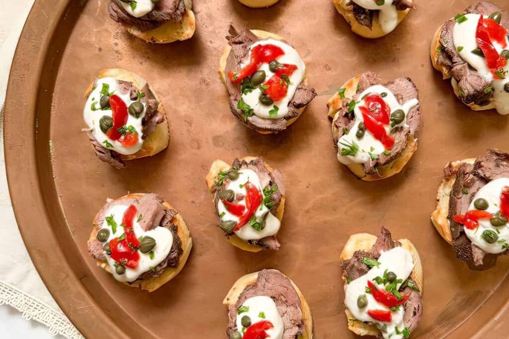 Steak tartines with horseradish cream arranged on a round tray.