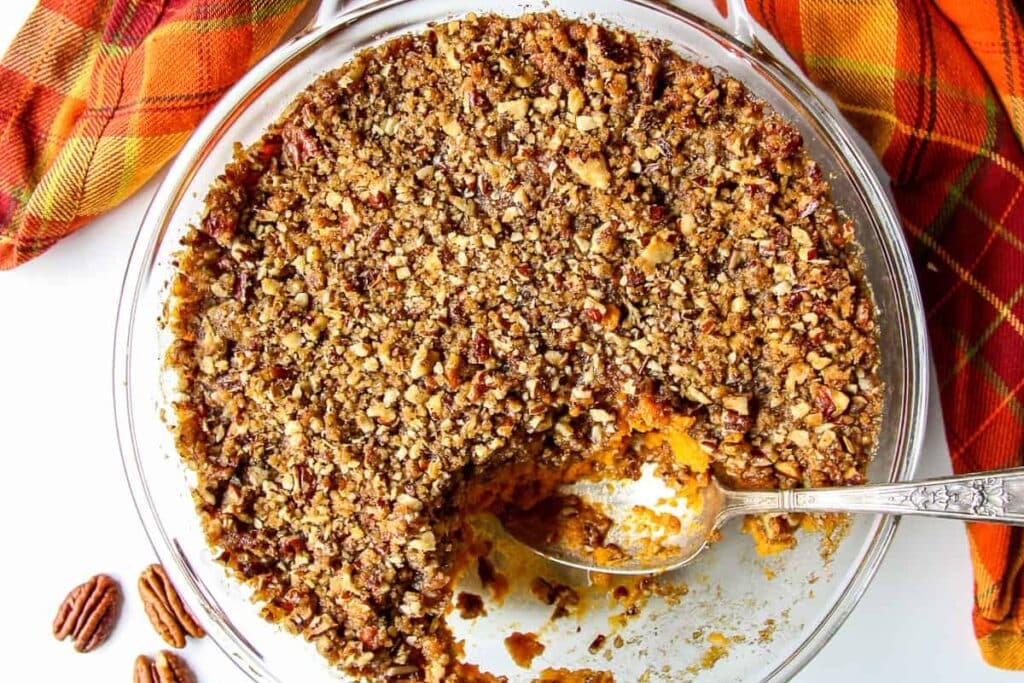 Sweet potato crunch in a glass baking dish with a spoon.