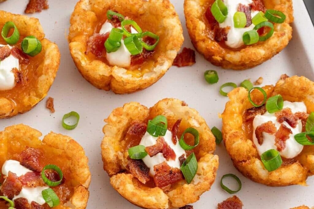 Tater tot cups filled with cheese and bacon, arranged on a white tray.