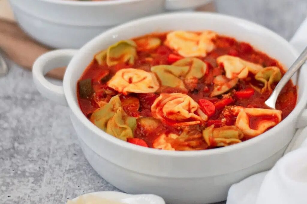 Tortellini soup in a white bowl.