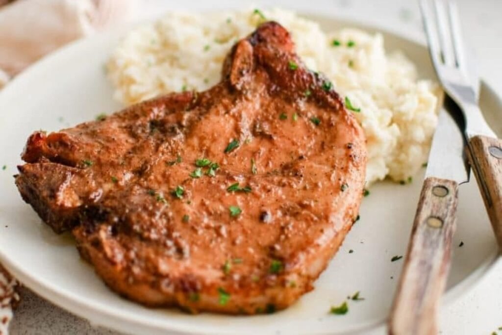 Baked pork chop with mashed potatoes on a white plate with silverware.