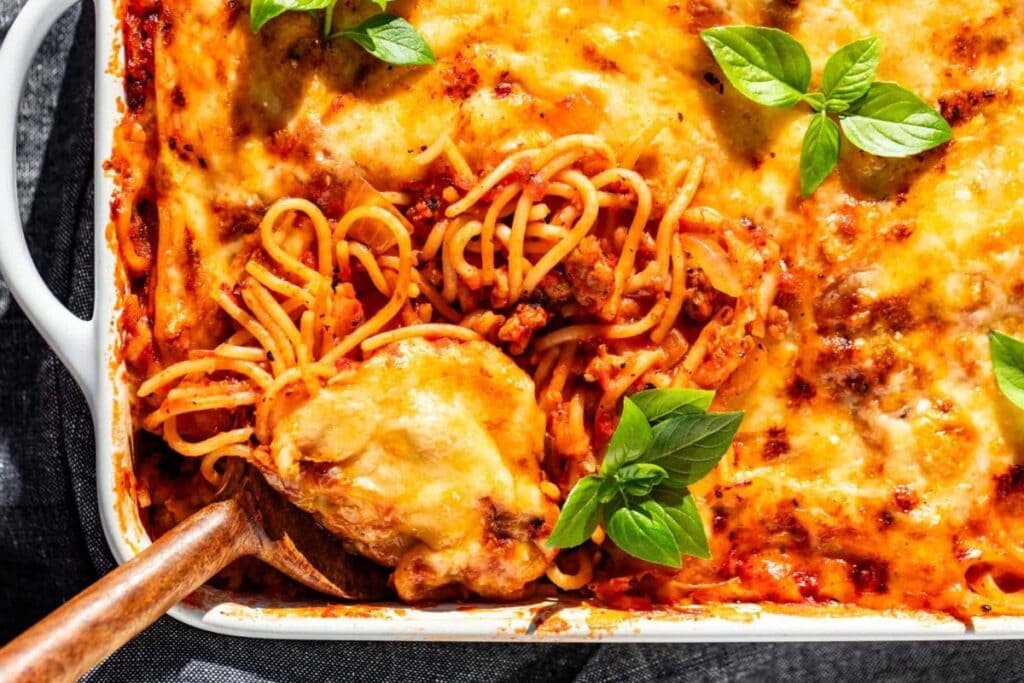 Baked spaghetti with meat sauce and cheese in a white baking dish.