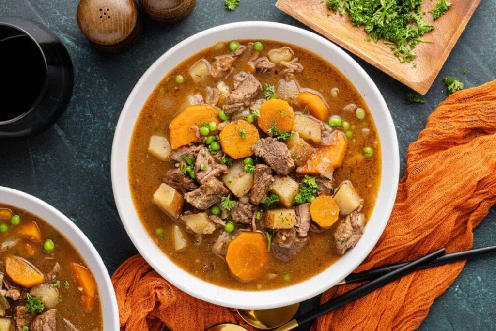 Beef stew with carrots, potatoes, and peas in a white bowl.