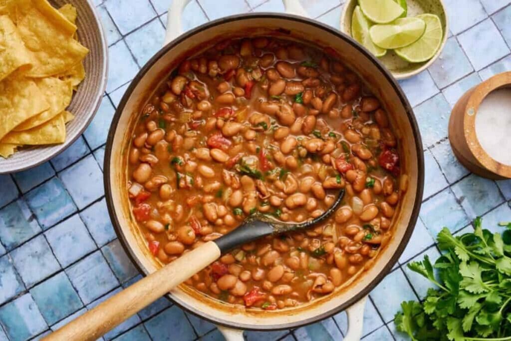 Overhead shot of charro beans in a pot with chips, limes, and cilantro.