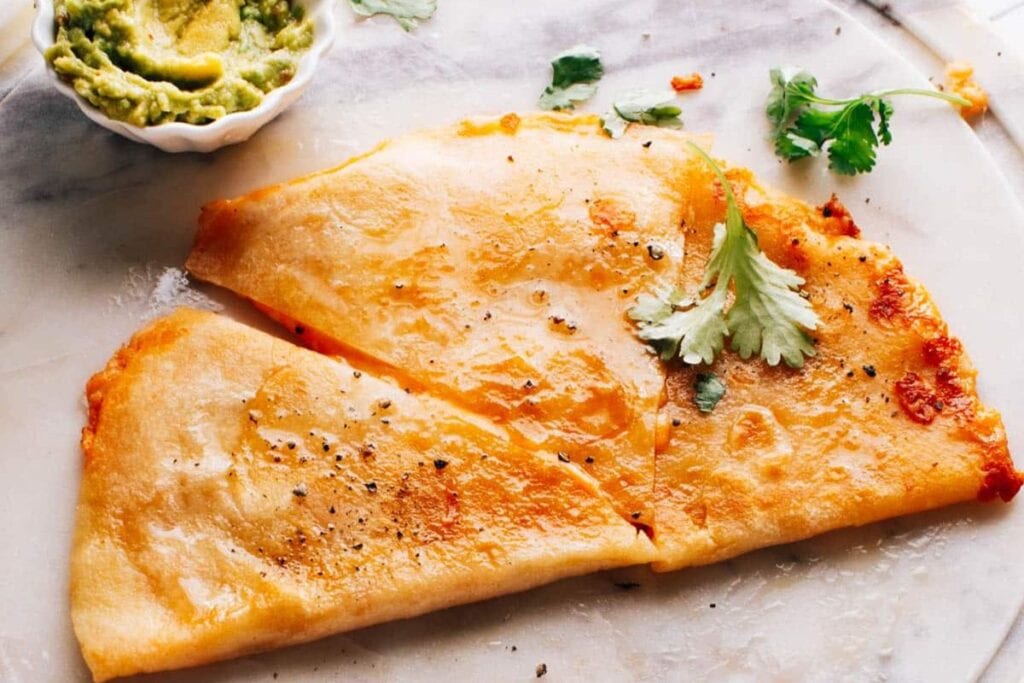 Cut cheese quesadilla with guacamole and cilantro on a marble board.