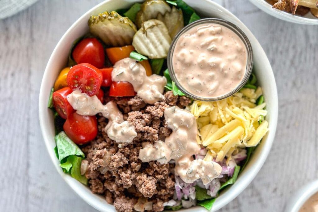 Cheeseburger bowl with ground beef, lettuce, tomatoes, pickles, cheese, red onion, and dressing.
