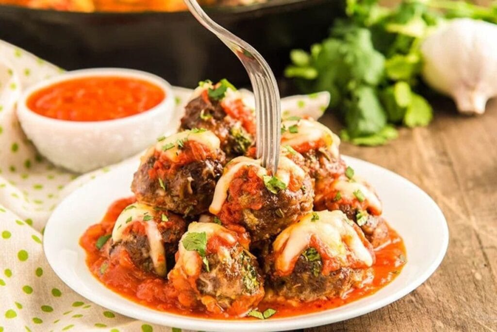 Cheesy meatballs with tomato sauce on a plate, pierced by a fork.