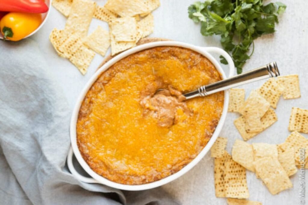 Cheesy refried bean dip in a white serving dish with crackers.