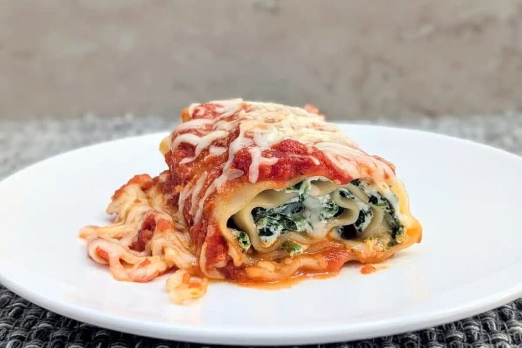 Side view of cheesy spinach lasagna roll-up on a white plate.