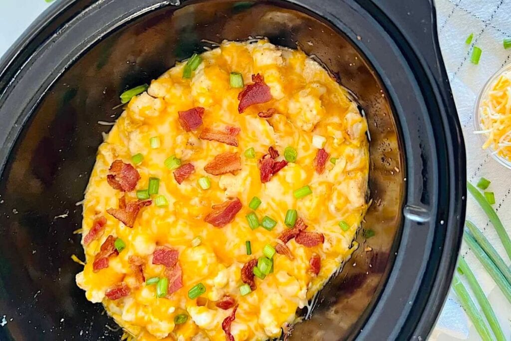 Overhead shot of chicken and cauliflower casserole with bacon in a slow cooker.