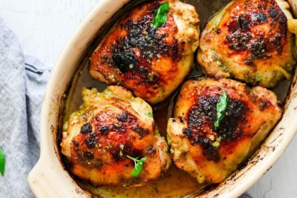 Four chicken thighs in a baking dish with basil.