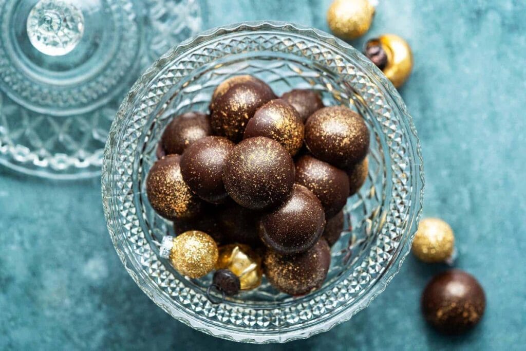 Chocolate cranberry truffles with gold shimmer in a crystal bowl, holiday ornaments around.