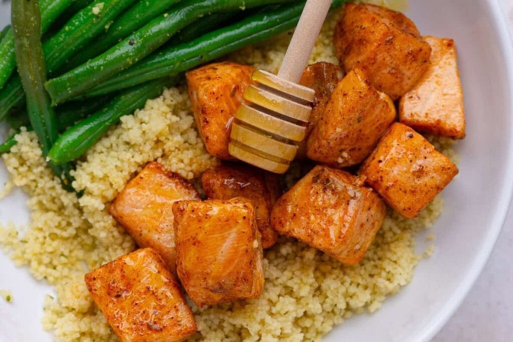 Salmon bites with hot honey, couscous, and green beans in a bowl.