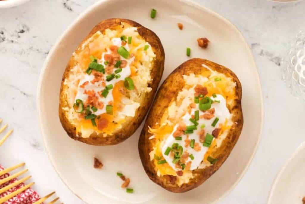 Two baked potatoes topped with sour cream, cheese, bacon, and chives.