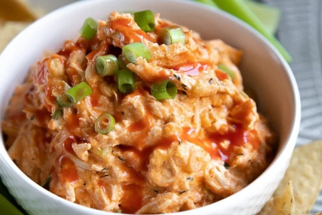 Buffalo chicken dip with green onion garnish and hot sauce drizzle.