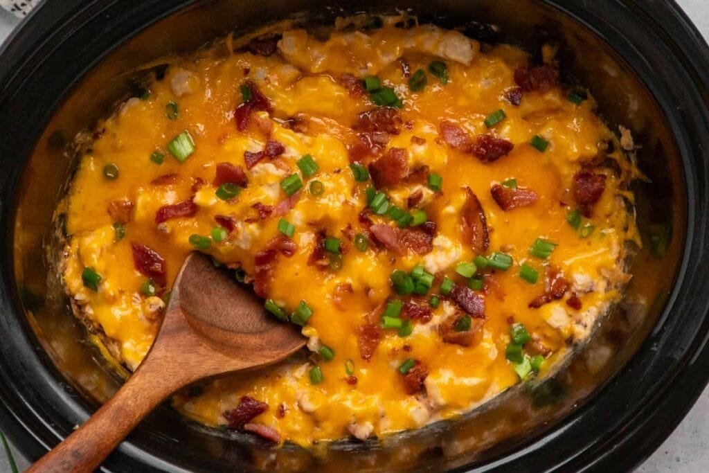 Crack potatoes with bacon and green onions in a crockpot with a wooden spoon.