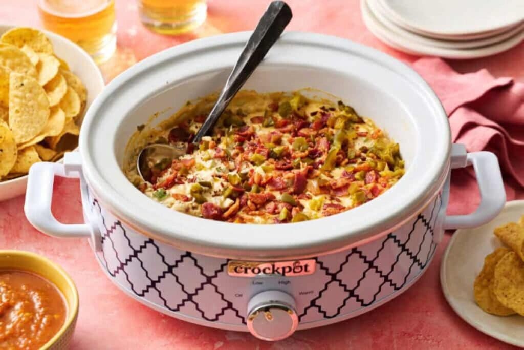 Jalapeno popper dip with bacon in a decorated Crock-Pot with chips and salsa.