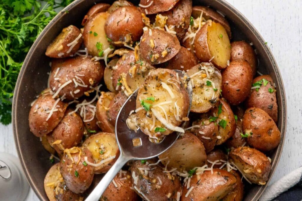 Bowl of roasted red potatoes with herbs and parmesan cheese, being served with a spoon.