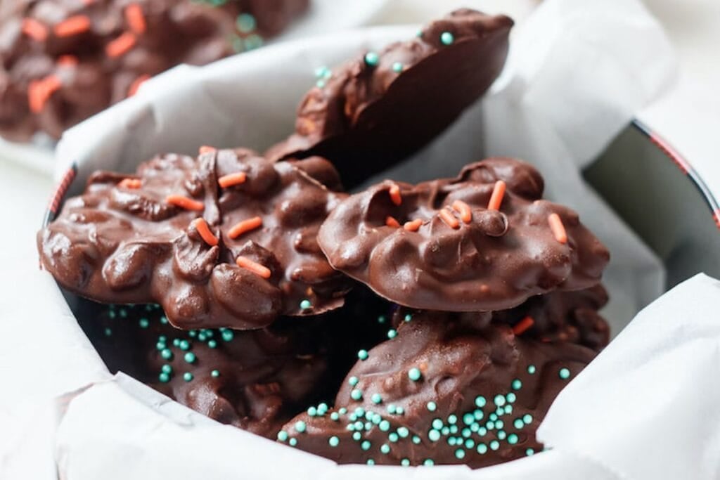 Chocolate crock pot candy with peanuts and sprinkles in a tin.