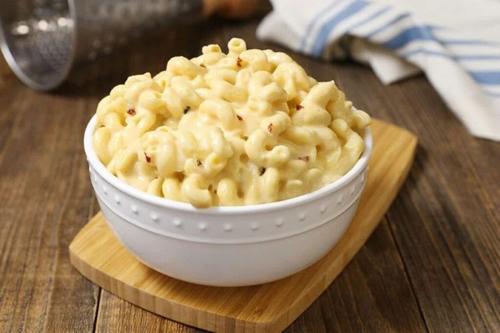 Mac and cheese in a white bowl on a wooden cutting board.