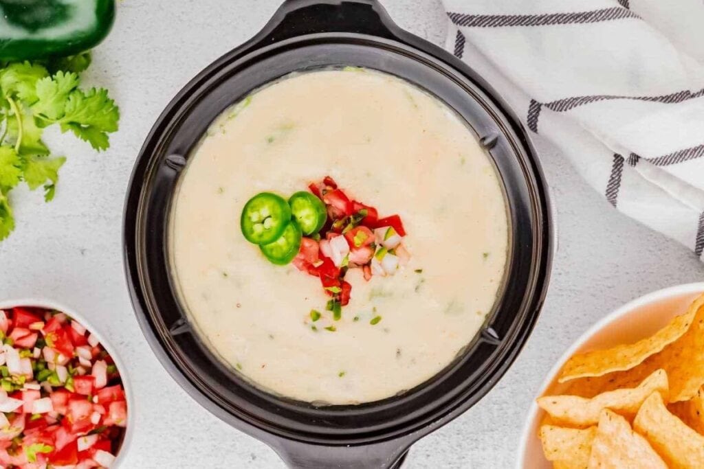Overhead shot of white queso dip with jalapeños, pico de gallo, and tortilla chips.