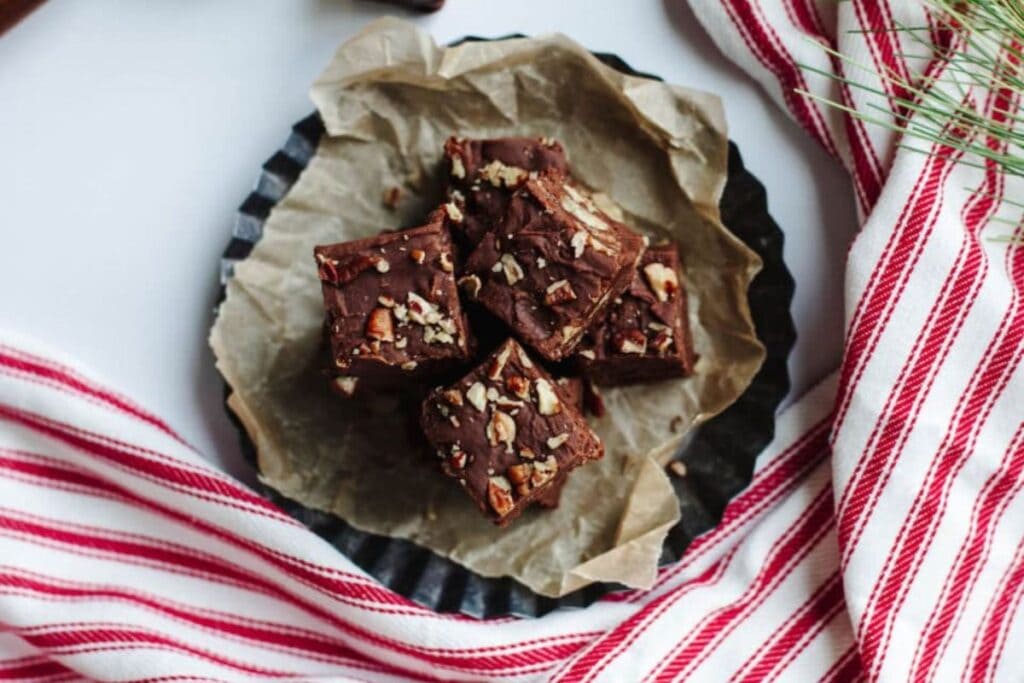 Chocolate fudge squares with nuts on parchment paper on a black plate.