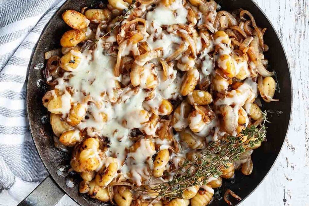 Overhead shot of French onion skillet gnocchi with melted cheese and thyme.