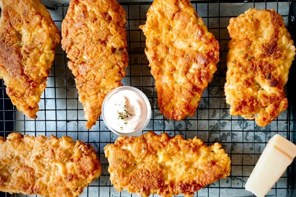 Crispy fried chicken breasts on a wire rack with dipping sauce.