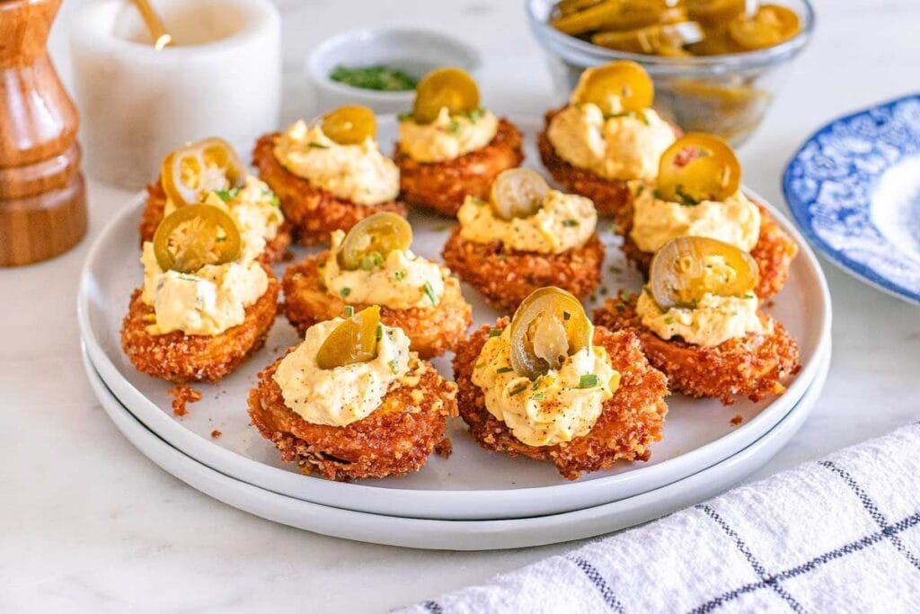 Fried deviled egg bites topped with pickled jalapeños on a plate.