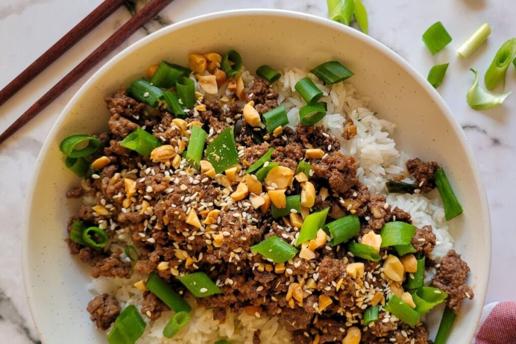 Bowl of rice topped with ground beef, peanuts, and green onions.