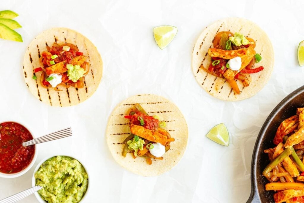 Overhead shot of halloumi fajitas with salsa, guacamole, and lime wedges.